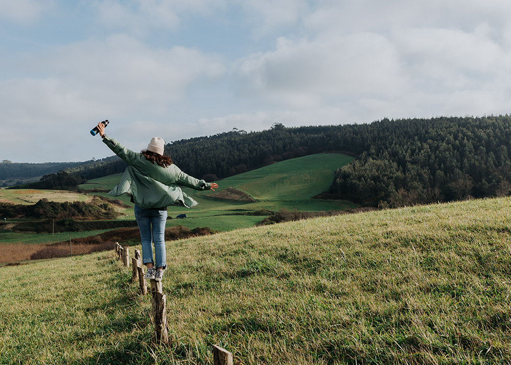 woman balancing on a fence in rural landscape