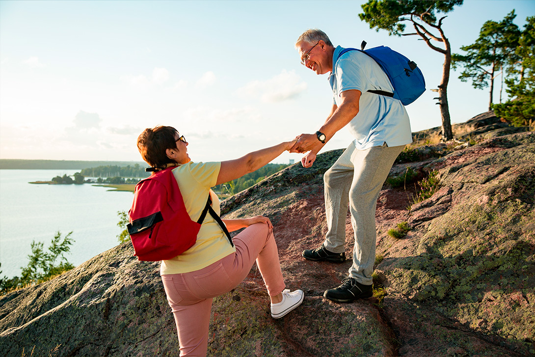 middle aged couple climbing a hill in the finnish archipelago, helping each other